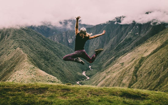 A woman jumping in the air on top of a mountain, promoting longevity through supplements.