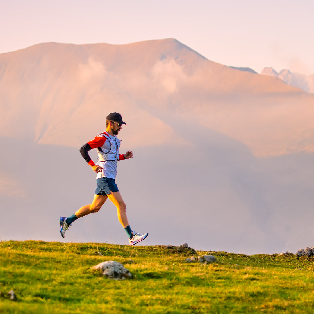 A person jogs on a grassy hill with mountains rising majestically in the background under a clear sky.