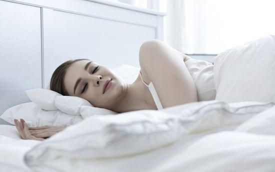 A woman is sleeping peacefully in a bed with soft white sheets.
